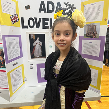 A student's dressed as Ada Lovelace in front of a display about her