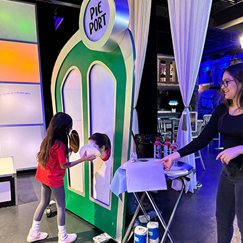 staff watching as a students puts a pie in the face of the student in the pie port