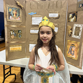 A student's dressed as Cleopatra in front of a display about her