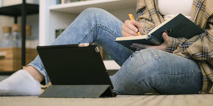 Girl writing in a notebook and looking at her tablet