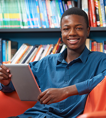 Male teen using a tablet computer in the school library