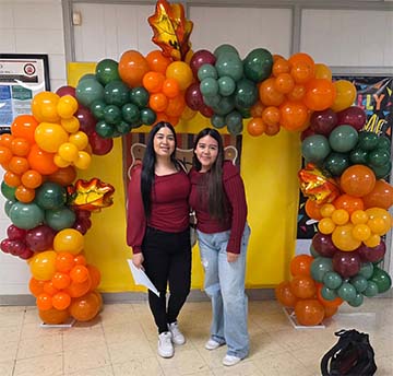 Two students under a balloon arch