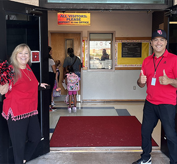 Two staff members greeting people as they wank through the school door