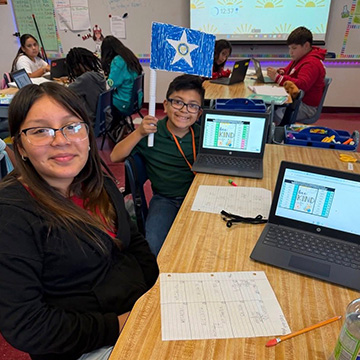 students working in a classroom, one is holding up a flag