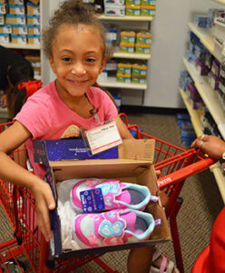 elementary student smiling at the camera while showing off her donated new pair of shoes