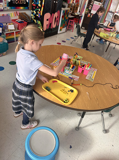 Kindergarten student making her own Rosary beads