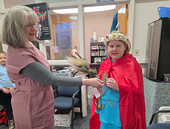 Student dressed in blue costume with red cape and a wreath of flowers