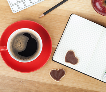 Red mug with coffee next to notepad with heart-shaped cookies