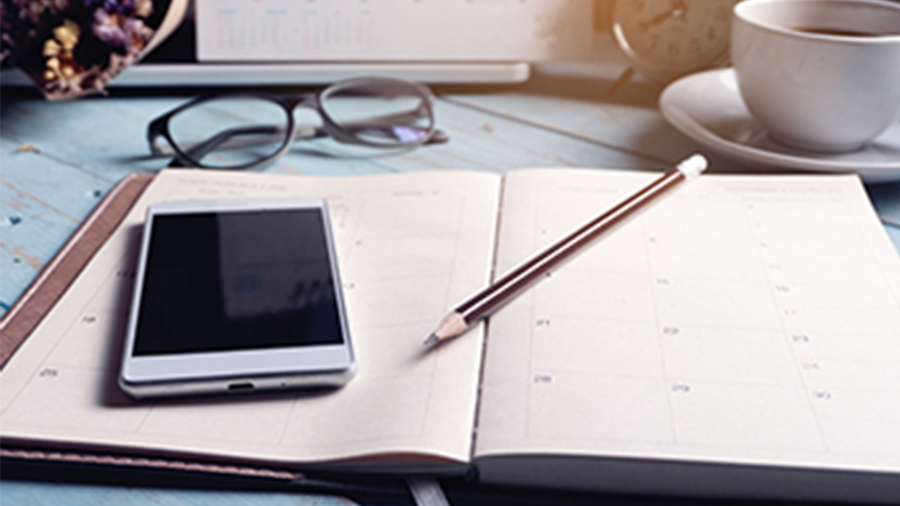 Monthly planner opened with laptop, cell phone, and pencil