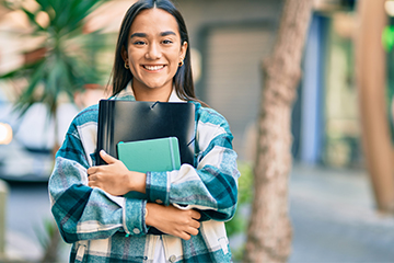 Female student outside holding books and smiling for the camera