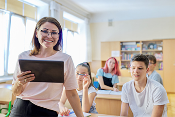 Happy teacher in her classroom holding a tablet computer