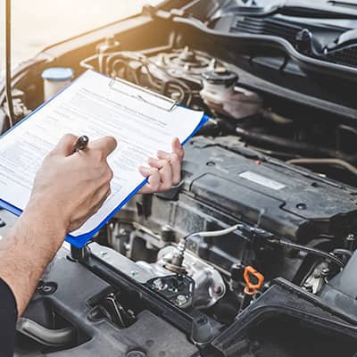 Person checking paper while examining a car engine