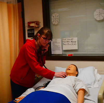 Student listening through a stethoscope for a heartbeat on a manikin