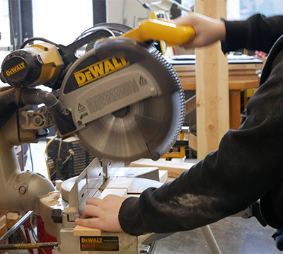 A student in a workshop cutting wood with a saw