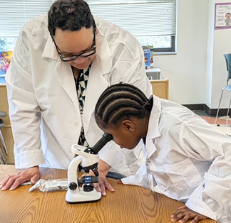 Teacher and student in lab coats using a microscope