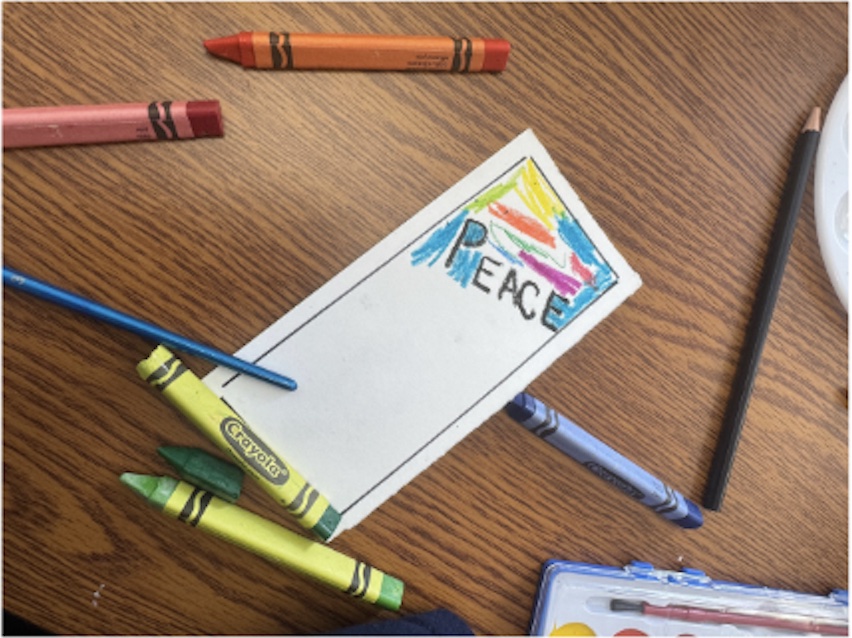 Assorted crayons on a table next to a PEACE notepad
