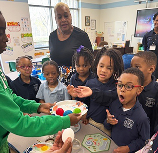 Group of students with a teacher watching someone dyeing eggs