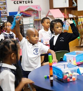 sidebargraphic_FAQ Two students in a classroom raising their hands