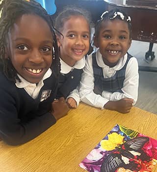 hree happy girls looking up from their desk in the classroom