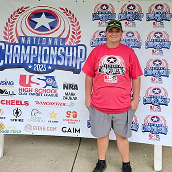 sidebargraphic-athleticsboosterclub student standing in front of a target national championship banner