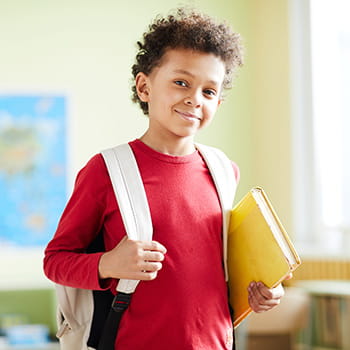 student with backpack on and book in hand