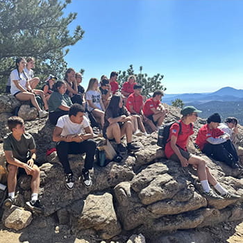 students sitting on top of a mountain looking out