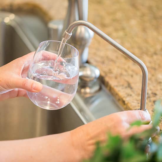 a person filling a glass of water at the sink