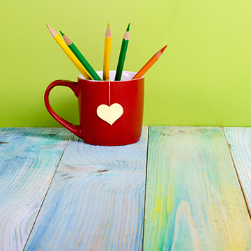Red coffee mug with colored pencils on table