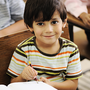 Happy elementary school boy looking up from his desk