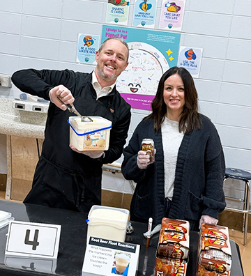 Two staff member making root beer floats at a school event