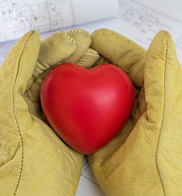 A red heart being held by someone wearing work gloves