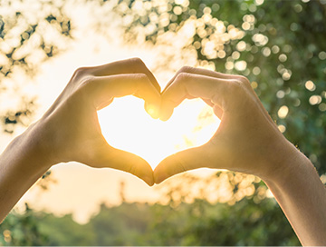 Hands in the shape of a heart in front of sun beam