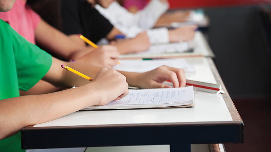 Students holding pencils and writing in notebooks on desks