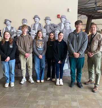 Staff and students lined up in front of a black and white mural of historic men