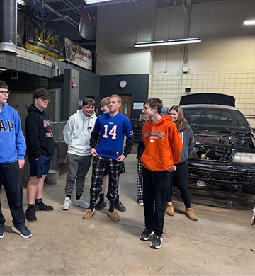 Students in a garage where they are working on a car
