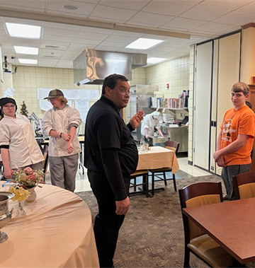 Students in a dining area listening to an adult