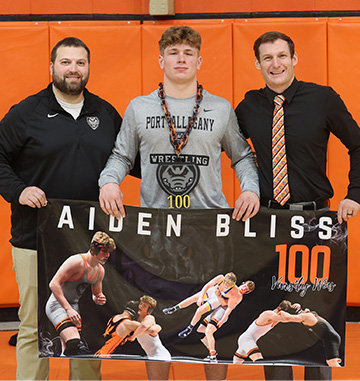 Aiden and two adults holding an Aiden Bliss banner showing pictures of him wrestling