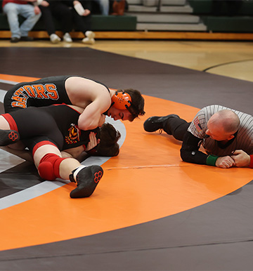 students wrestling and a referee on the ground watching