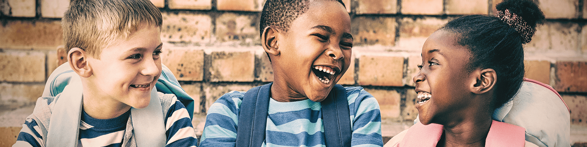 Three young diverse children laughing with each other