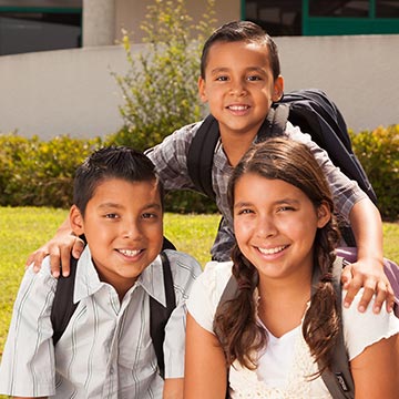 Three students smiling outside with their backpacks on Three students smiling outside with their backpacks on