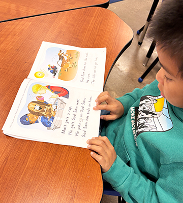 Young boy sitting at a desk reading a book