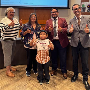 Student holding a certificate with staff members giving a thumbs up
