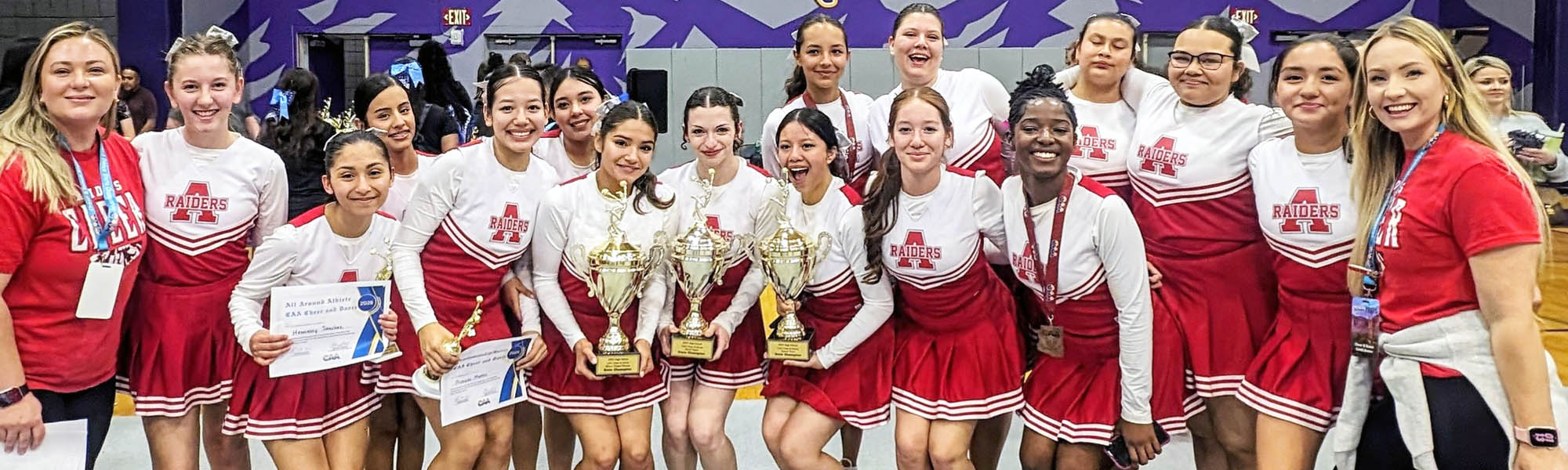 Cheerleading team and coaches proudly holding up three trophies