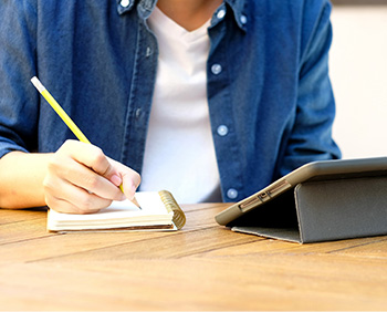 A student taking notes and looking at a tablet