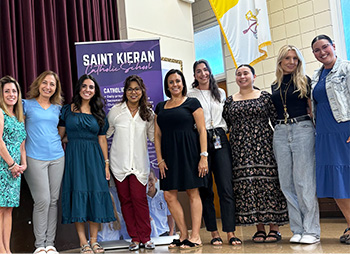 Group of happy staff members in front of a school banner