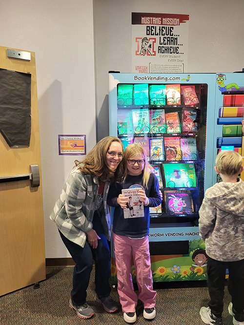 Woman and student holding up a book from the new book machine