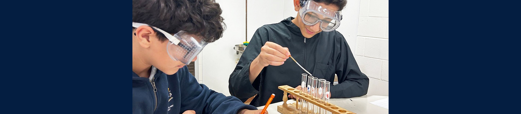 Two male students wearing safety goggles and working on a science project together