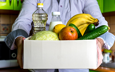 Woman holding up a box of food items for the local food pantry