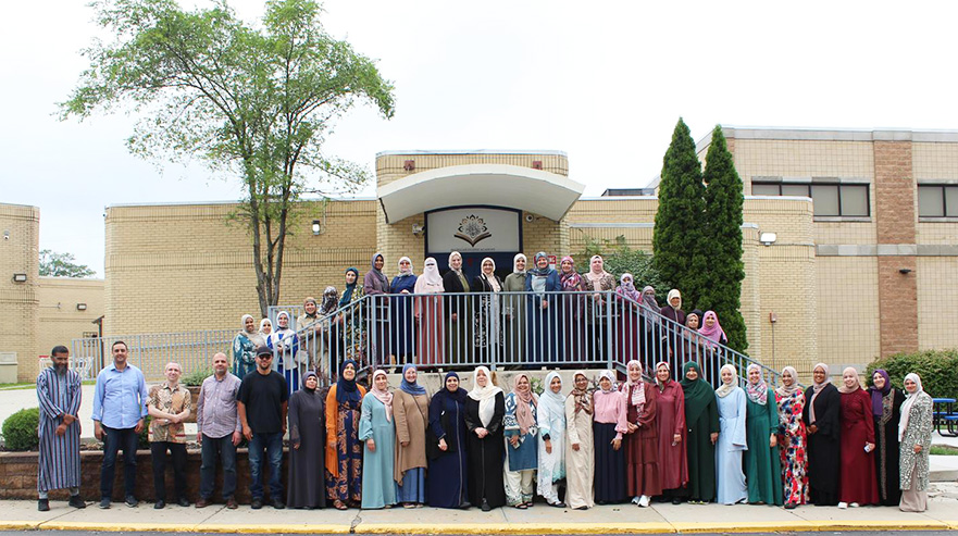 Group of happy staff members lined up around the front of the school building