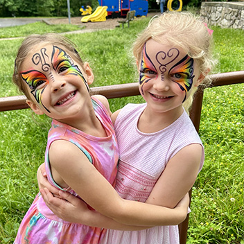Two happy girls smiling for the camera outside with their faces painted with butterfly designs